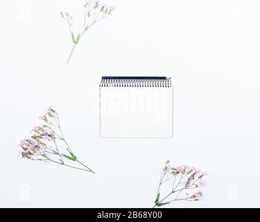 Flacher Lay Blumenmock-up aus leerem Notizblock unter rosafarbenen Blumen auf weißem Hintergrund, Draufsicht. Stockfoto