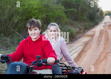 Zwei Teenager fahren auf einem Buggy, alle Geländewagen auf einer schlammigen Strecke. Stockfoto