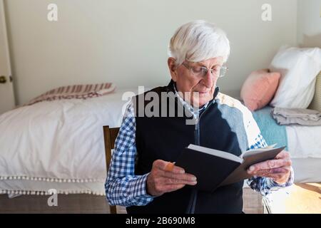 Der ältere Mann las ein Buch in seinem Schlafzimmer Stockfoto