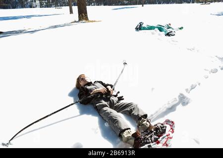 Ein sechs Jahre alter Junge, der Schneeschuhe trägt, liegt auf dem Rücken im Schnee Stockfoto