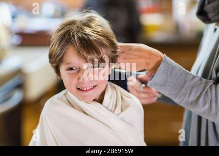 Ein sechs Jahre alter Junge, der von seiner Mutter zu Hause Haare schneiden ließ Stockfoto