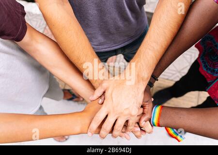 Hände einer Gruppe von Menschen verschiedener Ethnien mit einem lgtb-Flaggenarmband in der Straße zusammen Stockfoto