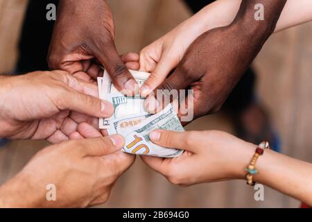 Einzelheiten zu den Händen einer Gruppe von drei jungen Menschen verschiedener Ethnien, die eine US-Dollar-Rechnung führen Stockfoto