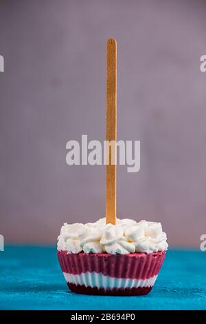 Erdbeer-Eis-Popsicle-Lollies mit Schlagsahne, die in Muffin-Formen auf graublauem Hintergrund gefroren ist. Stockfoto