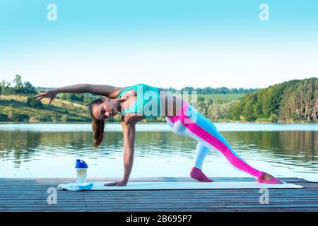 Schöne Mädchen üben Yoga auf dem Hintergrund der schönen Natur. Pilates. Gesundes Lifestyle-Konzept.Modell steht in Camatkarasana, Wild Thing oder Stockfoto