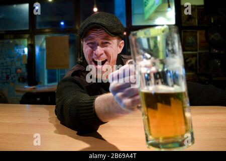 Der rothaarige, fast irischstämmige Kerl sitzt in der Bar und trinkt etwas Bier und schaut mit lustigen Gesichtern auf Sie und Jubele Stockfoto