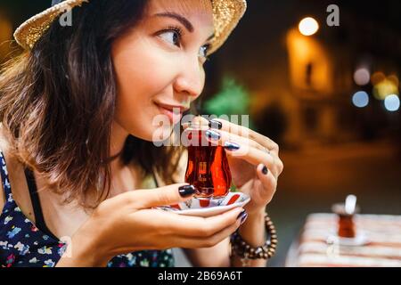 Frau Touristin trinkt nachts köstlichen traditionellen türkischen Tee im Café im Freien Stockfoto