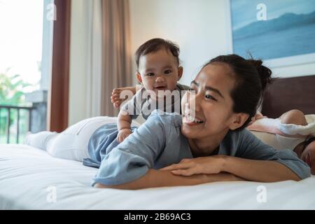 Mutter liegt mit ihrer Tochter im Bett, während sie im Schlafzimmer spielt Stockfoto