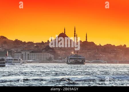 Passagierfähren und Schiffe transportieren Menschen vor dem Hintergrund einer Moschee und eines Sonnenuntergangs durch die Straße Bosporus in Istanbul Stockfoto