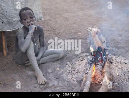 Mundari Stammjunge, der ein Lagerfeuer mit getrockneten Kuhdungs macht, um Fliegen und Stechmücken, Central Equatoria, Terekeka, Südsudan abzuwehren Stockfoto