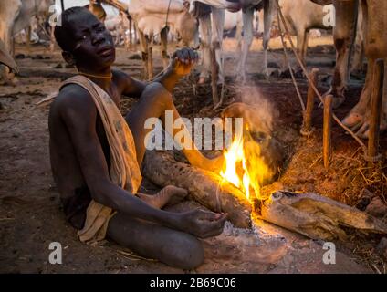 Mundari Stammjunge, der ein Lagerfeuer mit getrockneten Kuhdungs macht, um Fliegen und Stechmücken, Central Equatoria, Terekeka, Südsudan abzuwehren Stockfoto