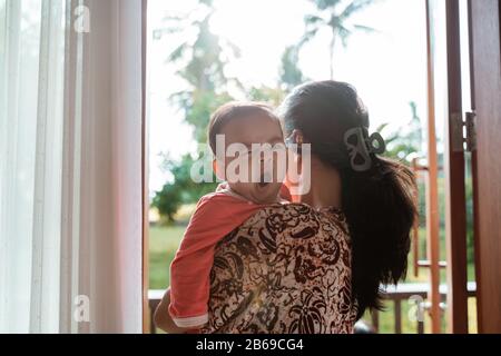 Asiatische Mutter, die ein schläfriges Baby hält, während sie vor der Tür steht