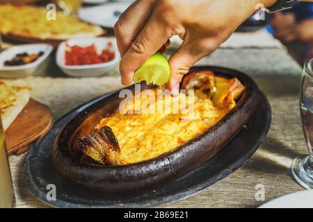 Appetitlich gebackene heiße Fisch-Süßwasserforelle ganz in einem Gericht auf einem Tisch in einem Restaurant mit frischer Zitrone oder Limette Stockfoto