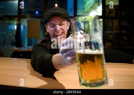 Der rothaarige, fast irischstämmige Kerl sitzt in der Bar und trinkt etwas Bier und schaut mit lustigen Gesichtern auf Sie und Jubele Stockfoto