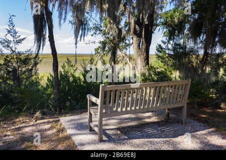 Holzbank auf Jekyll Island, Georgia. Entspannen Sie sich im Schatten der mit spanischem Moos bedeckten Eichen und genießen Sie den Blick auf den Salzwassermarsch. Stockfoto