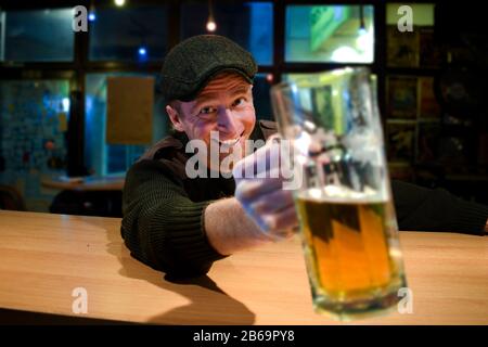 Der rothaarige, fast irischstämmige Kerl sitzt in der Bar und trinkt etwas Bier und schaut mit lustigen Gesichtern auf Sie und Jubele Stockfoto