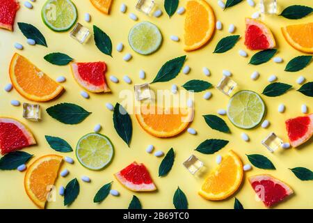 Muster aus Zitrusfrüchten, Limetten, Orangen- und Grapefruit-Scheiben, Minzkräutern, Eiswürfeln und frischen Pillen auf gelbem Hintergrund. Draufsicht. Minimaler Designhintergrund. Stockfoto