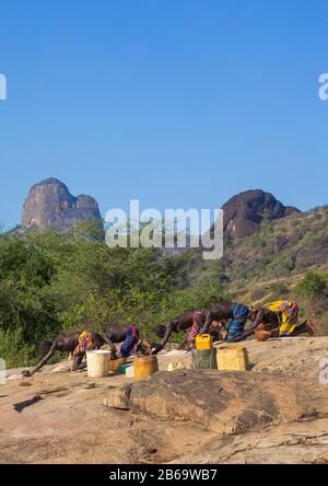 Larim-Stammfrauen mahlen Sorghum-Körner in Löchern in einem Felsen, Boya Mountains, Imatong, Südsudan Stockfoto