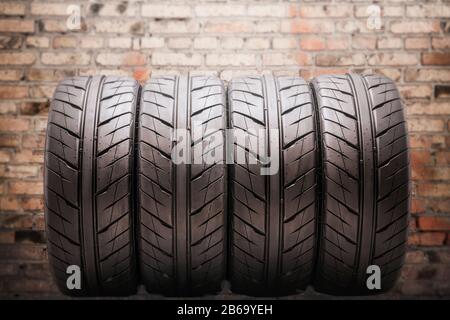 Vier Sommerreifen mit Drainageschlaufen, sehr schöner und moderner Safe, vor dem Hintergrund der Ziegelwand der Garage. Auto-Tuning und SPA Stockfoto