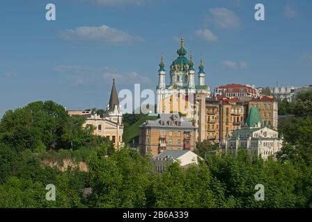 Allgemeiner Blick auf die Andrijivskyj-Abfahrt mit der Andreaskirche im Hintergrund. Grünes Laub im Vordergrund. Ort - Kiew, Ukraine. Stockfoto