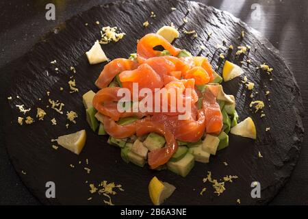 Tatar von Lachs und Avocado. Frischer Salat auf schwarzem Steinschiefer. Restaurant-Menü. Konzept für nährende organische Lebensmittel Stockfoto