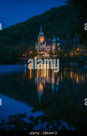 Beleuchtete Nordfront des Lillafured Palastes (Miskolc, Ungarn). Hamori-See mit Spiegelung im Vordergrund. Stockfoto