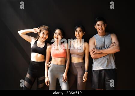 Fröhliche lächelnde Männer und Frauen, die Spaß haben, im Fitnessstudio zu sprechen. Gruppe junger Leute, die sich nach dem Training mit schwarzem Hintergrund im Fitnessstudio entspannen. Stockfoto
