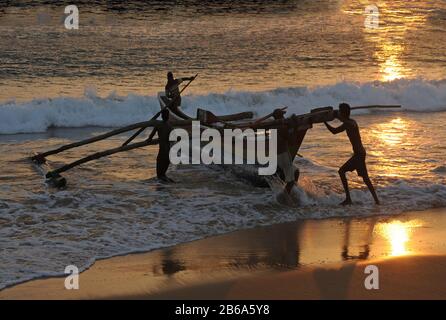 Holzfischboot beginnt am Meeresstrand. Szene bei Sonnenuntergang. Es werden nur Silhouetten von Menschen gesehen. Stockfoto