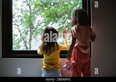 Zwei kleine Kinder, die aus dem Fenster sehen, wenn sie im Schlafzimmer stehen Stockfoto