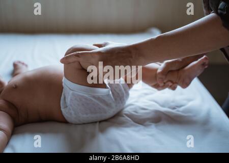 Die Mutter hält die Füße eines Kleinkindes im Bett liegend und massiert Stockfoto