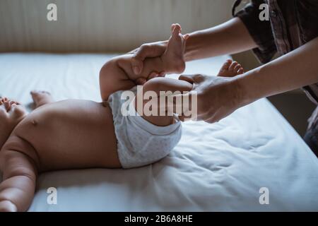 Mutter streckt ihre Babyfüße auf das Bett und gibt Massage Stockfoto