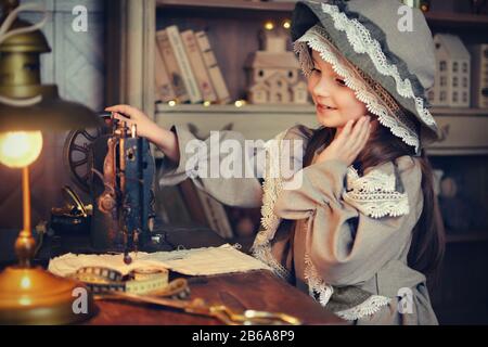 Schönes kleines Mädchen im Retrokleid mit einer Kappe näht auf einer Nähmaschine. Retro-Stil. Verarbeitung. Stockfoto