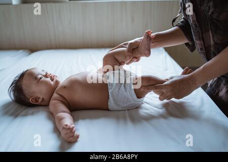 Die Mutter hält die Füße eines Kleinkindes im Bett liegend und massiert Stockfoto