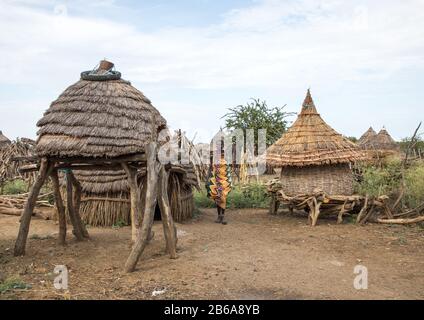 Toposa-Stammfrau, die in der Nähe von Getreidegranaten in einem Dorf, Namorunyang State, Kapoeta, Südsudan, vorbeikommt Stockfoto