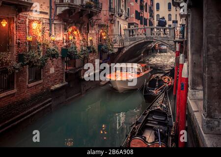 Ein venezianisches Wassertaxi fährt unter einer kleinen Brücke auf einem schmalen Kanal in Venedig, Italien Stockfoto