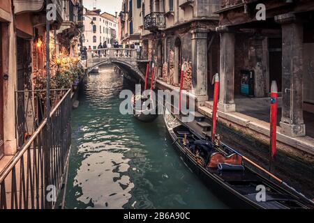 Gondeln auf einem schmalen Kanal in Venedig, Italien, mit einer kleinen Brücke im Hintergrund und einer Weihnachtsbeleuchtung gegenüber Stockfoto