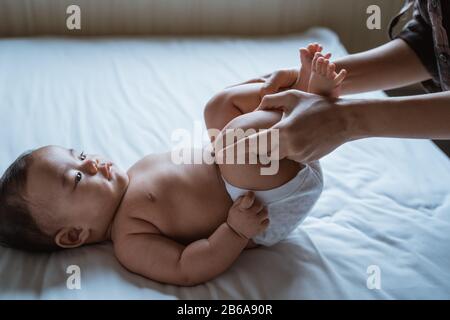 Mutter streckt ihre Babyfüße auf das Bett und gibt Massage Stockfoto