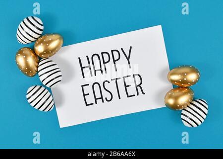 Schwarz-weiße und goldene Ostereier mit weißer Karte mit "Happy Easter"-Text auf blauem Hintergrund Stockfoto