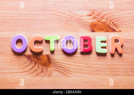 Oktoberwort mit bunten Buchstaben auf Holzhintergrund, Draufsicht Stockfoto