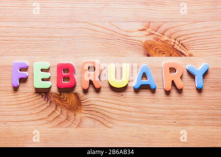 Februarwort mit bunten Buchstaben auf Holzhintergrund, Draufsicht Stockfoto