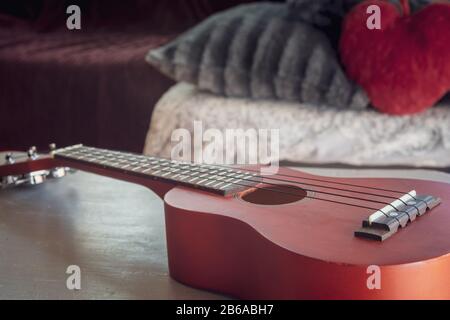 Rote Ukulele auf dem Tisch mit gemütlichem Zimmer im Hintergrund Stockfoto