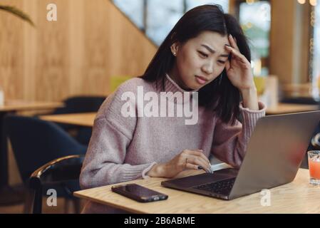 Das peinliche Mädchen arbeitet in einem Laptop in einem Café und ist mit den Fehlern unzufrieden. Verwirrte Geschäftsfrau ärgert sich über Online-Problem, Spam-E-Mail oder gefälschte Internet-Nachrichten auf dem Laptop. Arbeitsantin fühlt sich schockiert über festgefahrenen Computer, verwirrt durch Betrug oder Virus. Stockfoto