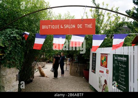 Leute, die unter dem Zeichen eines Boutique-Ladens und eines Teesaals mit französischen Flaggen in Giverny in der Nähe von Claude Monet House und Gardens.Giverny.France stehen Stockfoto