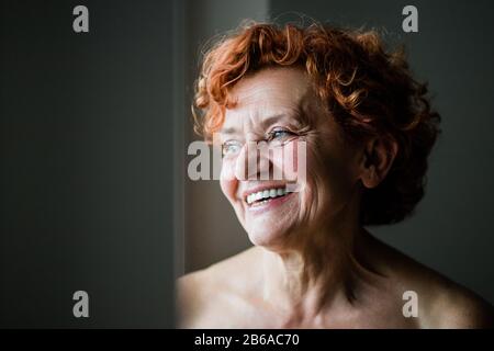 Fröhliche reife Frau lächelt am Fenster Stockfoto