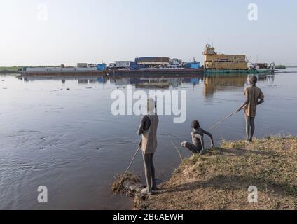 Barge, der vor dem mundarischen Stammjungen vorbeigeht, der im Nil, in Zentraläquatoria, Terekeka, im Südsudan fischt Stockfoto