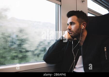 Junger Mann, der mit dem Zug unterwegs ist und Ohrhörer trägt Stockfoto