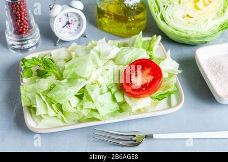 Wecker und Platte mit grünem Eisberg Salat, Tomatoe, Olivenöl, intermittiertem Fastenkonzept, Ernährung, Gewichtsverlust Stockfoto