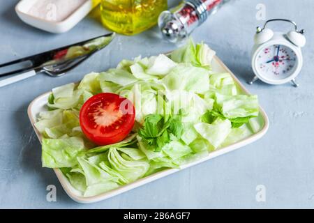 Wecker und Platte mit grünem Eisberg Salat, Tomatoe, Olivenöl, intermittiertem Fastenkonzept, Ernährung, Gewichtsverlust Stockfoto