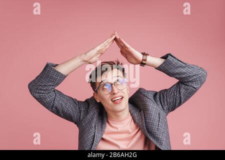 Porträt eines jungen attraktiven Mannes, der eine Jacke trägt, die isoliert über dem rosafarbenen Hintergrund steht und die Hände über dem Kopf hält Stockfoto