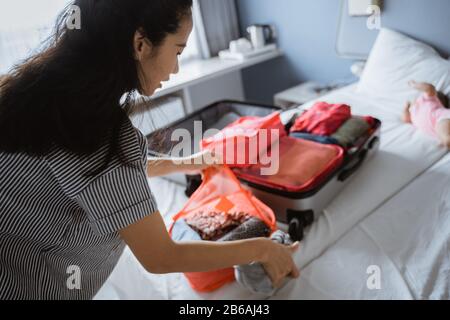 Asiatische Mutter bereitet Kleidung und Taschen für Urlaubsreisen vor Stockfoto